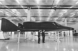 Men stand next to a sleek, black spaceplane